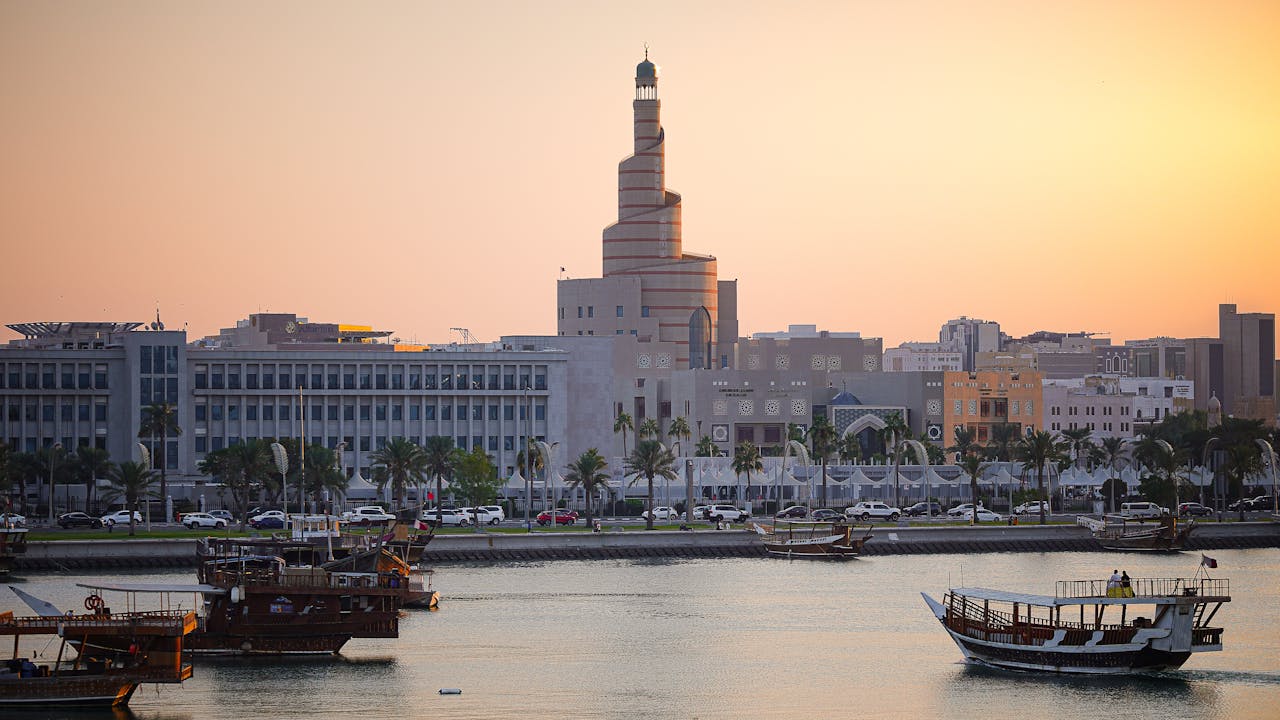 services-01 Scenic view of Doha's skyline at sunset with traditional boats on calm water.
