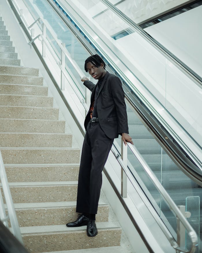 services-img Fashionable young man in a dark suit standing on a staircase indoors.