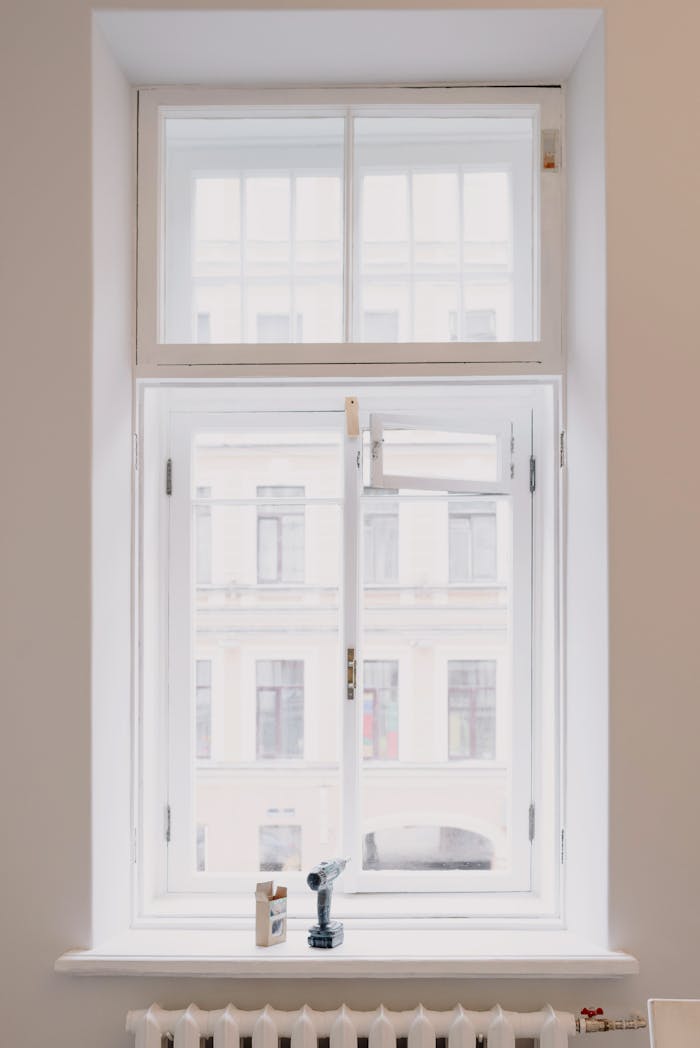 services-04 Wooden window with white frame overlooking building in city installed in light room with battery and screwdriver on windowsill in apartment