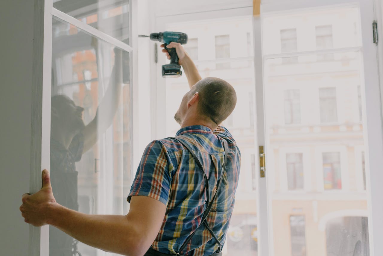 our-experience Back view of worker in checkered shirt drilling window frame during renovation process in apartment
